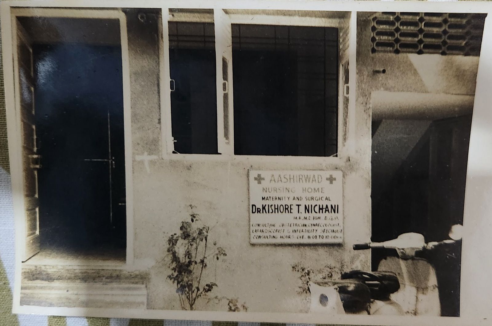 Archival black and white photograph of the original Aashirwad Nursing Home board — Maternity and Surgical, Dr. Kishore T. Nichani