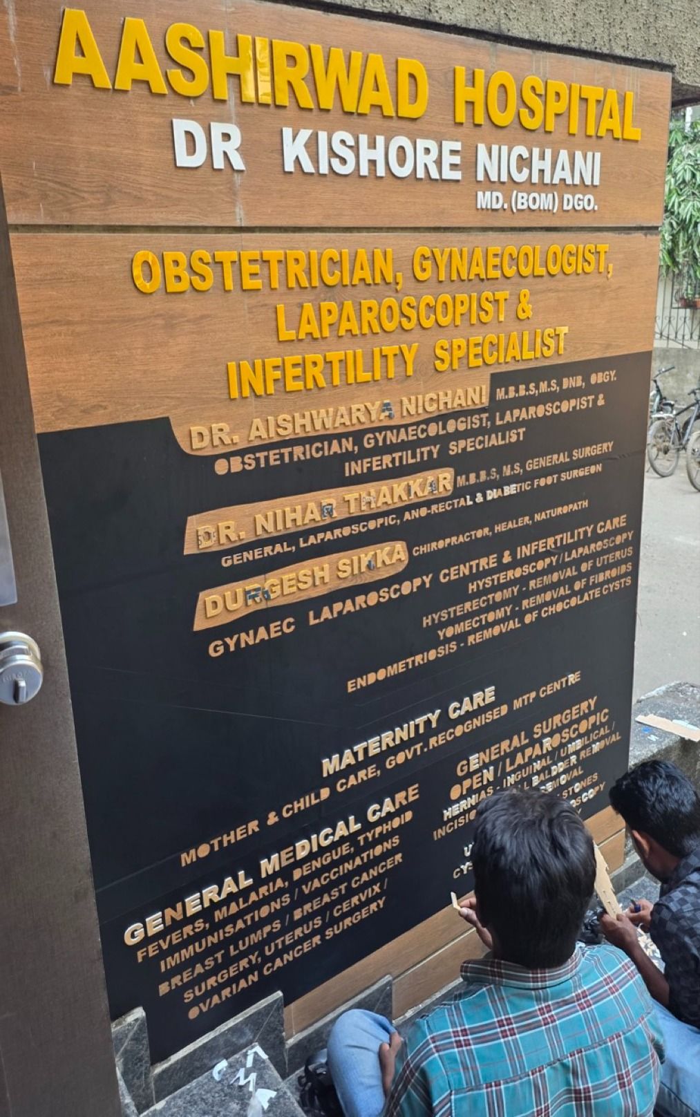 Sign painters adding Dr. Aishwarya Nichani's name to the Aashirwad Hospital board in 2025